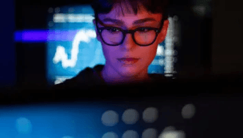 Person focused on monitors displaying financial charts and data in low light.